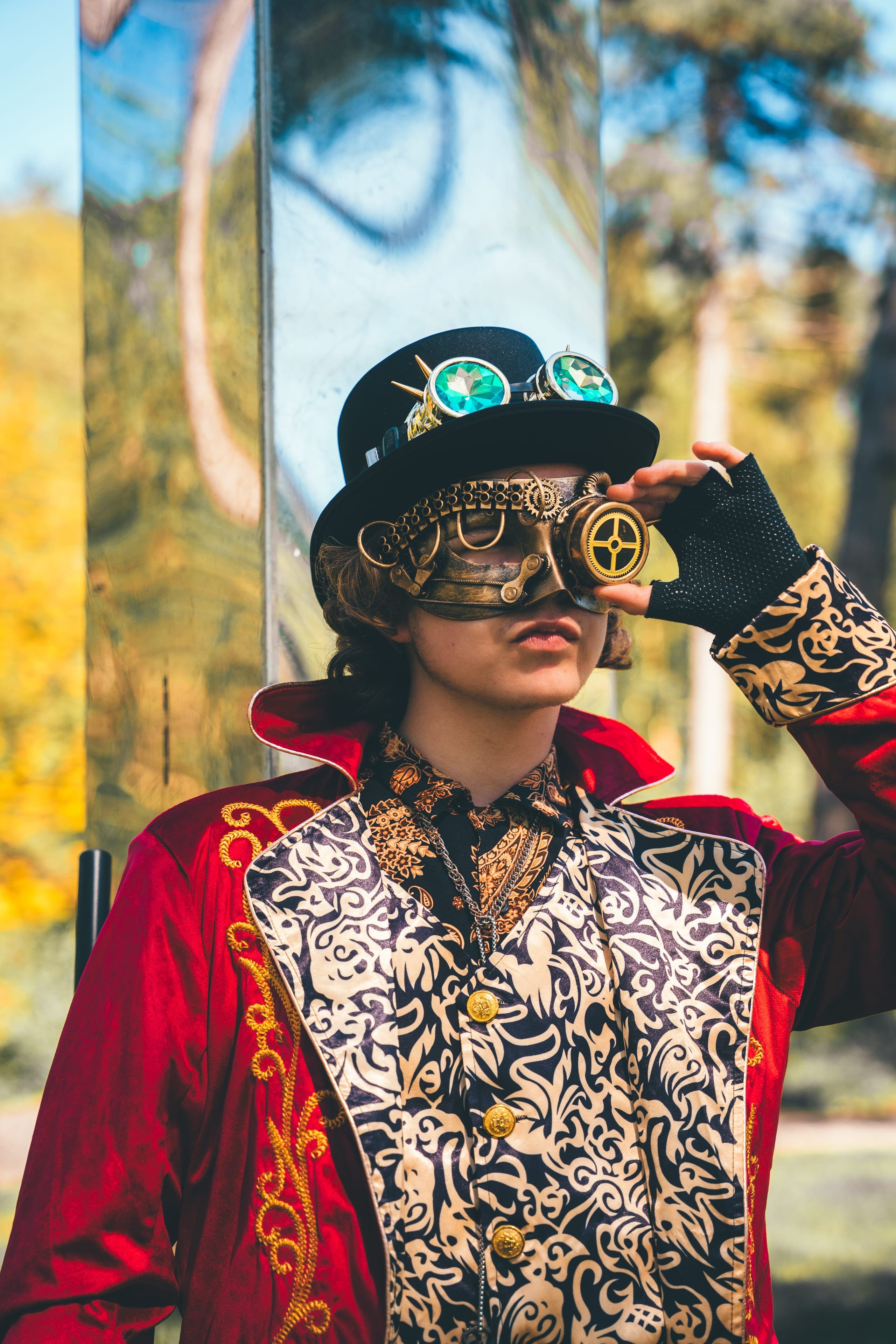 The Machinist, guardian of the Factory Realm: a red tailcoat, a brocade waistcoat and a brass-goggled top hat, photographed in the pines.