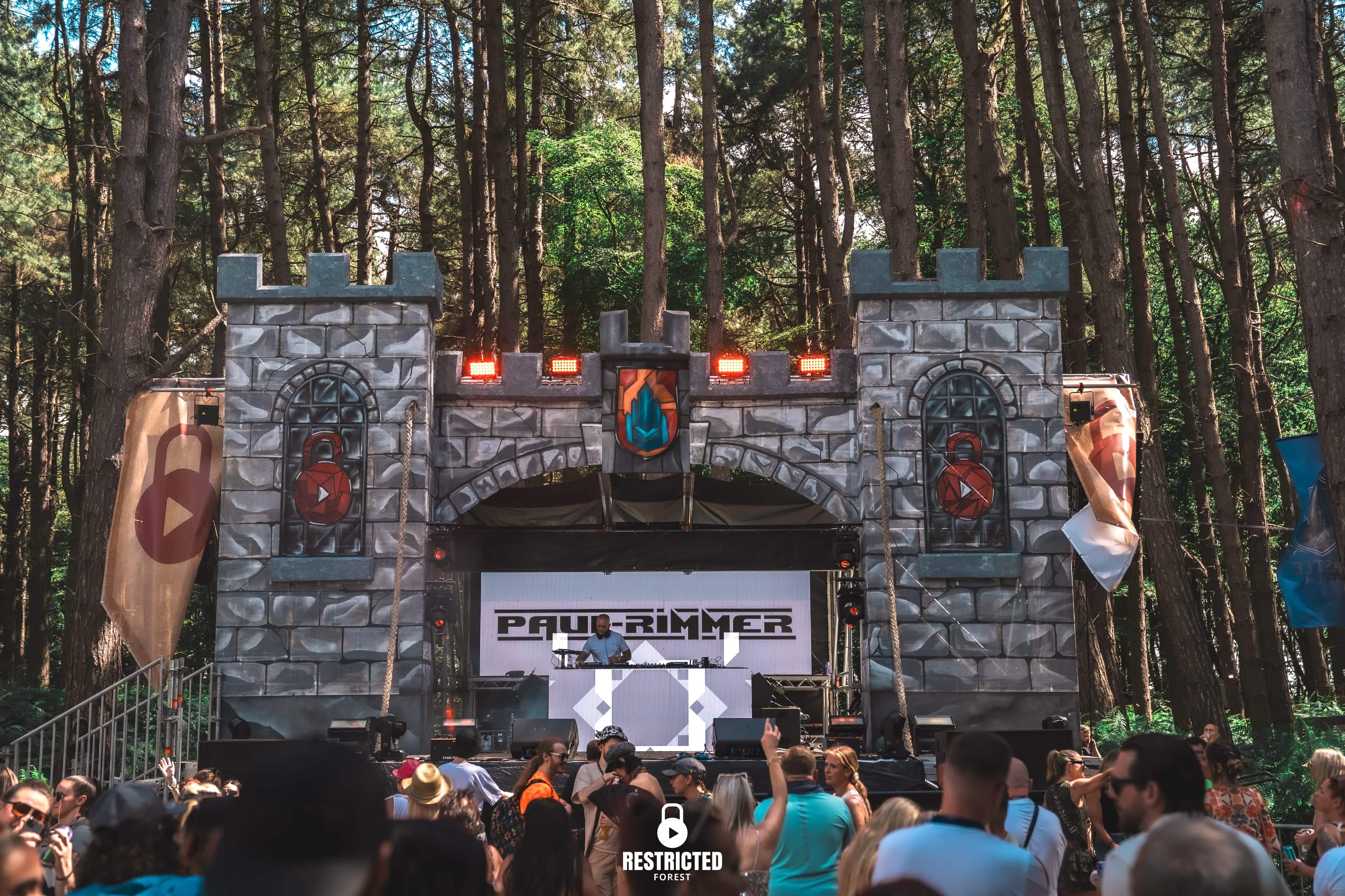 The stone castle stage set among the pines with the crowd gathered in front of it.