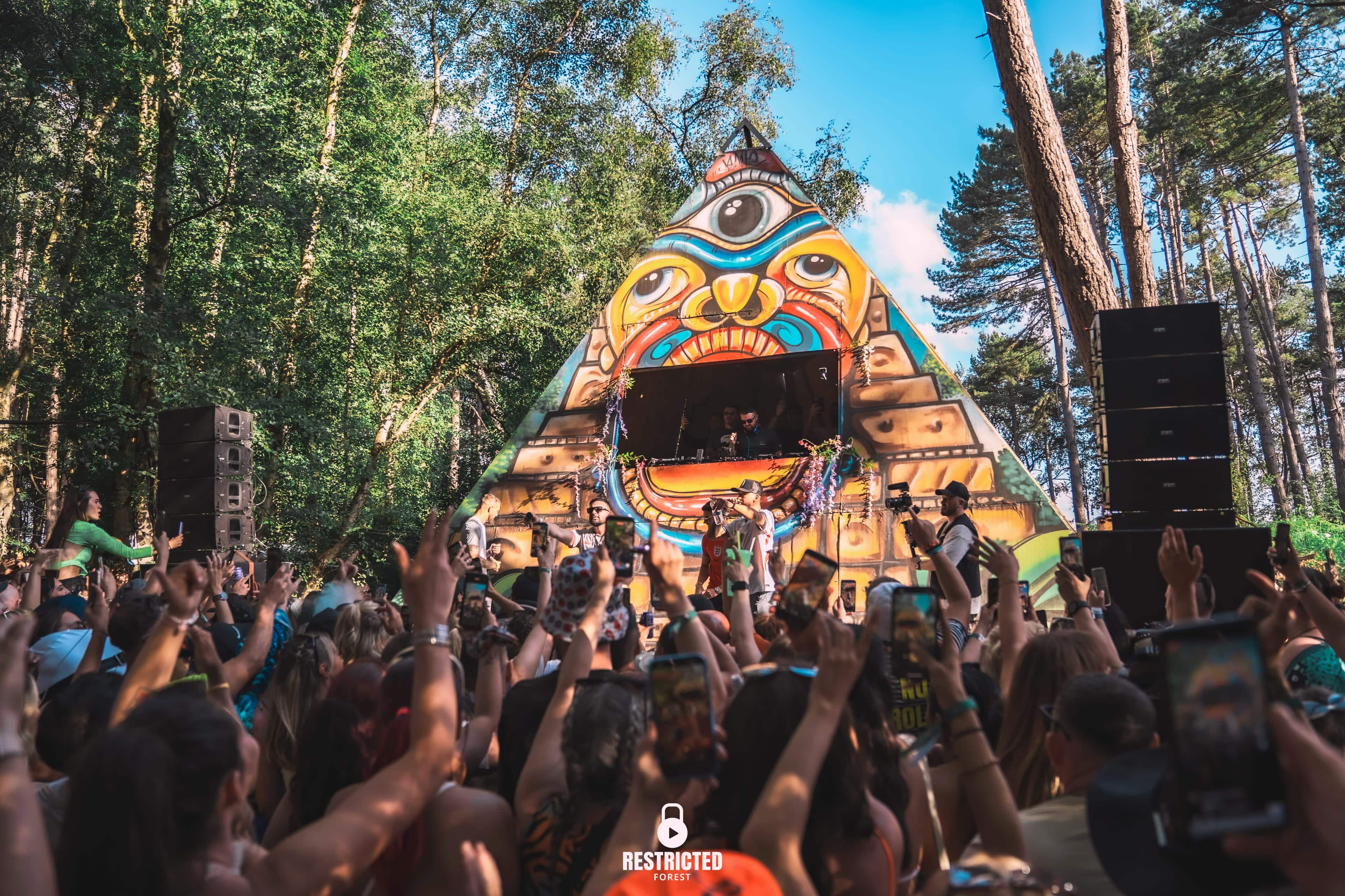 The painted pyramid stage under a clear sky, arms up across a full crowd.